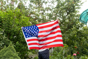 Positive attractive american young guy wrapped himself in the flag of America and looks at the camera, outdoors