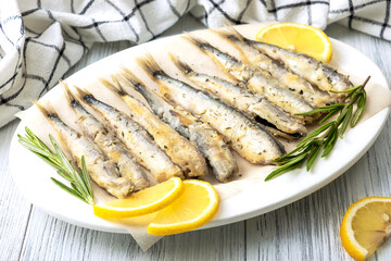 Close-up top view fried capelin on a white porcelain dish with lemon, rosemary and spices. Healthy food concept. Selective focus.