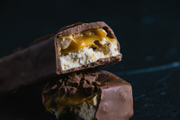 Delicious chocolate bar with caramel and peanuts close up on dark concrete background with copy...
