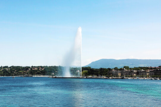 Geneva fountain Jet d Eau on Geneva lake against the background of the cityscape and mountains.