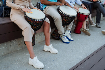A group of people play drums on the streets of the city, hands beat the rhythm on the djemba,...