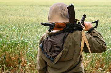 A soldier with a machine gun stands in a field, Ukrainian wheat fields and war.