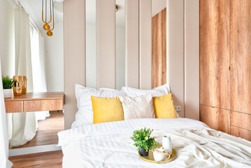 Luxury hotel room with double bed with white sheets and yellow pillows and wooden wardrobe. Modern interior with stylish design.