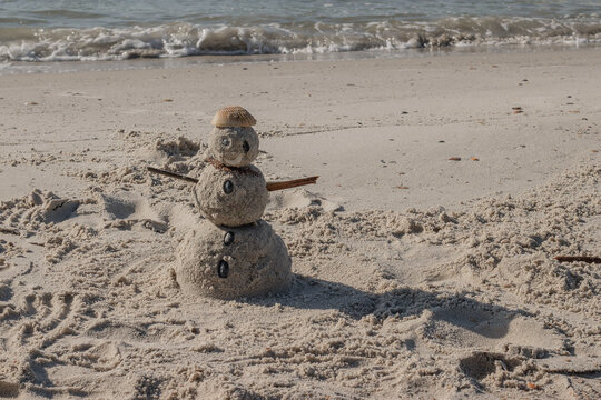 white sand snowman on beach with water and shells and sticks 