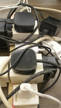 Vertical video social media format – Closeup of man’s hand using an overloaded, UK 240 volt electricity supply extension board, with a mess of adaptors, plugs, wires and cables.