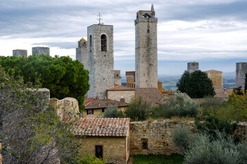 Fototapeta premium Medieval towers of the San Gimignano of Siena. San Gimignao towers under cloudy sky with stone wall houses and trees. Region of Tuscany, Italy.