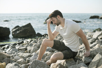 Depressed sad young man sitting on a sea beach