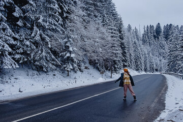 Woman on empty road through mountain forest with pines covered with snow
