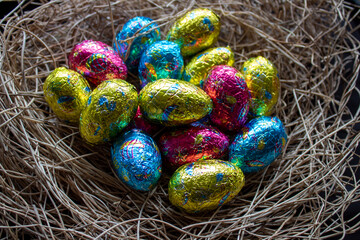 Un nid d'herbes sèches rempli de petits oeufs en chocolat emballés dans un papier de multiple couleurs