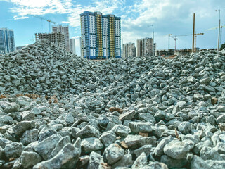construction of a new microdistrict in the city center. tall, high-rise buildings made of concrete and glass next to a pile of stones. stones for road construction