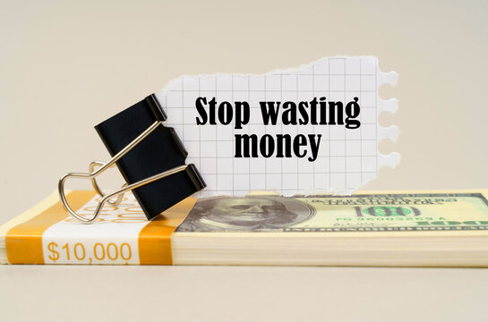 There are dollars on the table, on which there is a clip and torn paper with the inscription - Stop wasting money