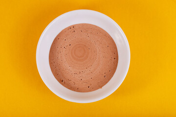 Tijela branca com sorvete de chocolate derretido, sobre mesa amarela 