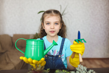 girl in blue t-shirt and yellow gloves with green watering can, paws and rake at home