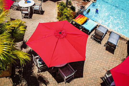Summer weekend at the country club with bright red sunbrellas and palm trees and turquoise swimming pool surrounded by lounge chairs - View from above