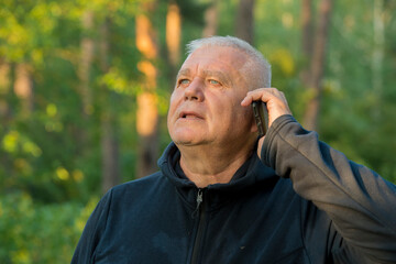 senior man uses the phone on the background of the forest