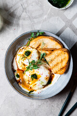 Cilbir or Turkish Eggs. dish served as mezze: poached eggs topped over herbed greek yogurt, then drizzled with hot spiced paprika olive oil. Turkish breakfast in a grey bowl on marble background