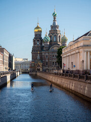 Obraz premium The Cathedral of Our Savior on the Blood under clear sky. People are sailing on SUP surfers.