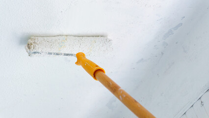 Someone painting wall with paint roller. Painting rough apartment wall, renovating with fresh white...