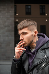 Street male portrait of a handsome brutal hipster man with a tattoo on his neck in fashionable...