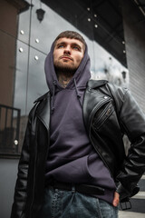 Fashionable handsome man model hipster in stylish clothes with a rock fashion black jacket and hoodie walking in the city