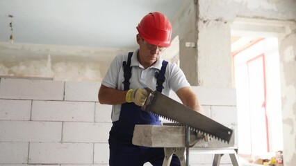 Bricklayer worker sawing foam concrete block with hand saw. Contractor cuts autoclaved aerated concrete blocks on construction site. Concept of building your own home.