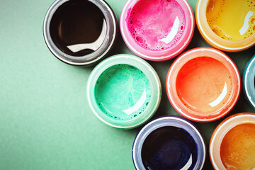 Bright, mother-of-pearl, multicolored open cans of paint on a bright green background. View from above. The concept of creativity.