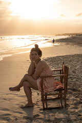 young woman sitting in a chair on the shore of the beach watching the sunset
