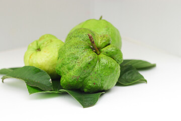 a group of fresh ripe Crystal guava (Psidium guajava) on green leaves isolated on white background.