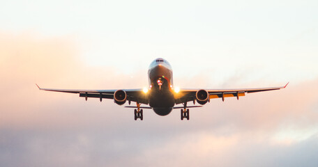 The silhouette of a passenger plane coming in for landing against the backdrop of the sunset sky.