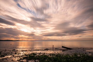 Long exposure view of shore of Trasimeno lake Umbria, Italy with trunks beneath a spectacular sky with moving clouds