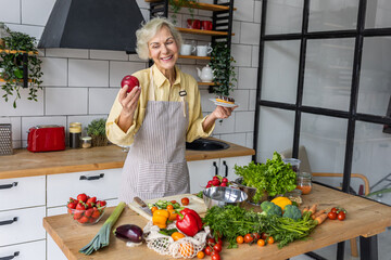 Attractive smiling senior woman with apple and donut, looking happy and healthy. Concept of active lifestyle of mature people, organic food. Female at home preparing vegetarian salad, holding a cake