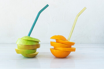 Refreshing drink from whole apple and orange with glass straws. Drinks are without glass directly from fruits. Refreshing healthy concept, dieting. Lots of copyspace.