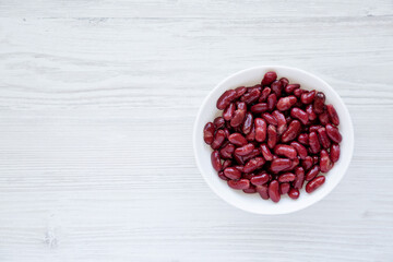 Red Organic Kidney Beans in a White Bowl on a white wooden background, top view. Flat lay, overhead, from above.