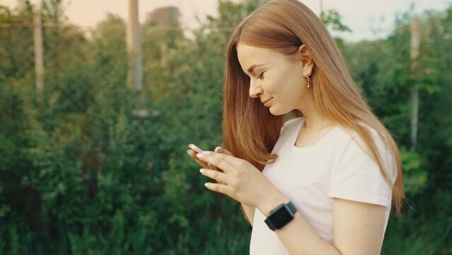 Portrait of a beautiful girl typing on a mobile phone while walking in the park