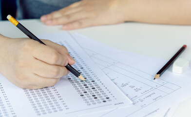 Students hand holding pencil writing selected choice on answer sheets and Mathematics question sheets. students testing doing examination. school exam