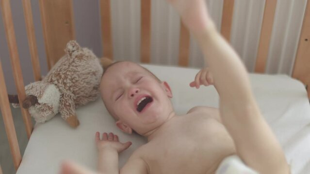 portrait of crying screaming naked baby infant, lying sitting in crib cot cradle. caucasian toddler child in panties doesn't want to sleep, kid yelling, overreacting or go into hysterics 