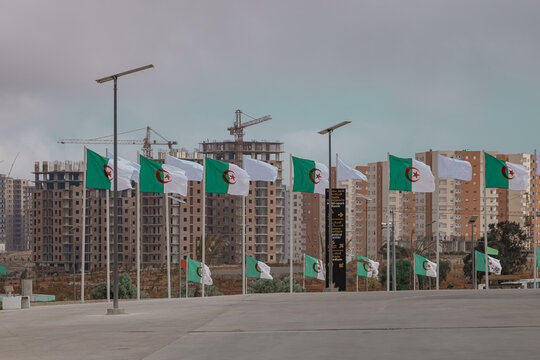 Algerian flags waving in the wind in front of residental block under construction. Visible cranes and unfinished buildings in the city of Oran.