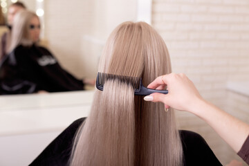 
Hairdresser's hand brushing long silver blonde hair in beauty salon
