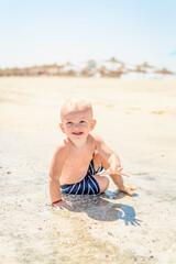 happy child boy laughing and sitting on beach by sea
