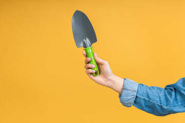 Close-up photo of green shovel in woman's hand isolated over yellow background.