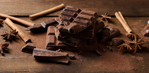 broken pieces of dark chocolate, cinnamon sticks and star anise on a brown wooden table, top view