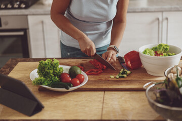 Process of cutting fresh vegetables for a salad by woman standing at a table for cooking in kitchen