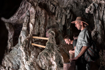 Two young friends wearing a hat are having fun exploring a cave and looking down from the heights