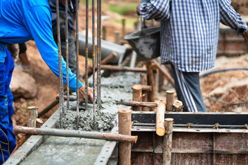 Construction workers are pouring wet concrete from mixer trucks into building foundations at a high-rise construction site.