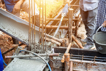 Construction workers are pouring wet concrete from mixer trucks into building foundations at a high-rise construction site.