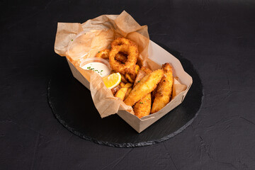 Beer snacks, squid rings, cheese sticks, French fries, on a black background, side view