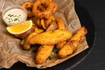 Beer snacks, squid rings, cheese sticks, French fries, on a black background, side view