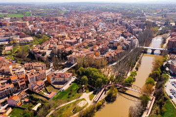 Scenic drone view of modern residential areas of Aranda de Duero city on banks of Duero river on sunny spring day on background of natural rural landscape, Burgos, Spain - obrazy, fototapety, plakaty