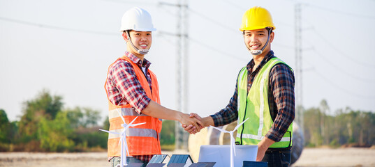 Two engineers shaking hands in construction site and Electric power line and pole