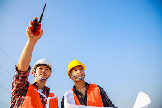 Two Engineers Point To The Construction Site Project. Teamwork, Leadership. Clean Sky In Background